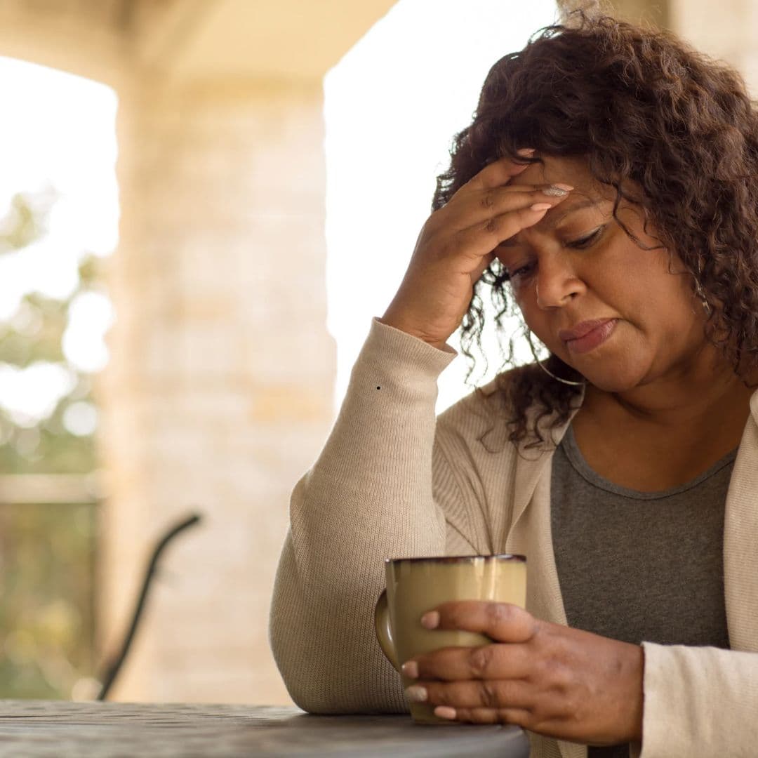 A woman sitting outside with a cup of coffee, resting her head in her hand.